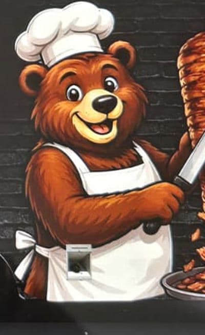 The Beärlin bear chef in an apron and toque, carving döner from the spit.